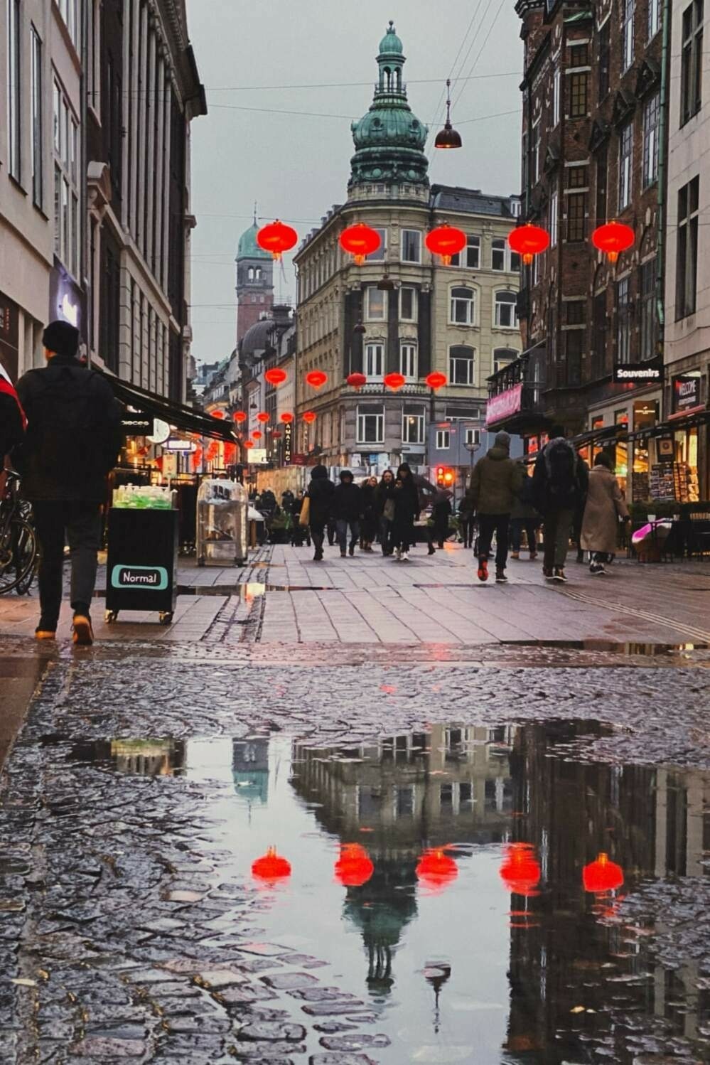 A pedrestrian street with puddles reflecting the red Chinese lantens hung overhead.