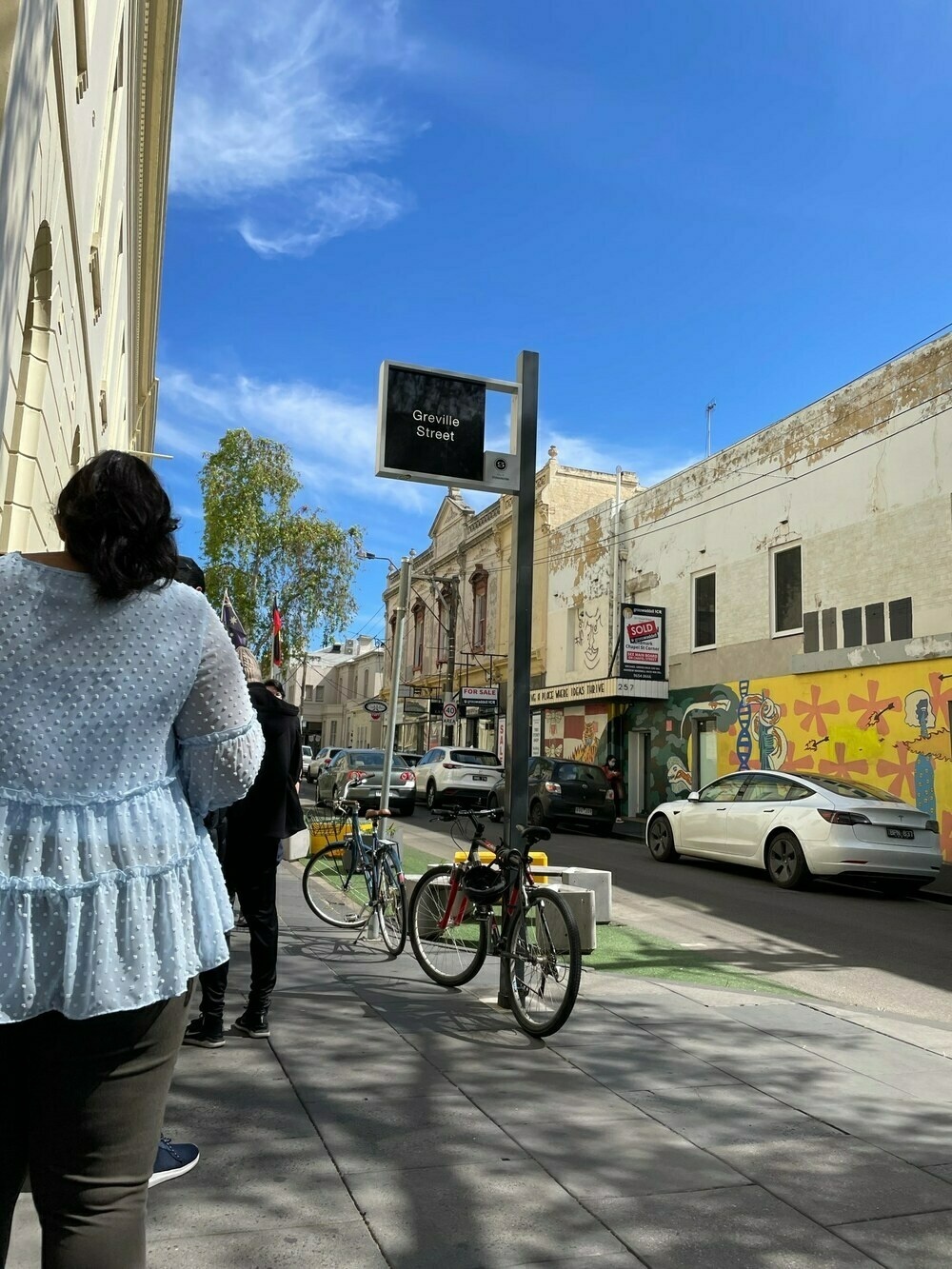 Greville St Prahran, with a queue of waiting people, a mural and a road devoid of traffic
