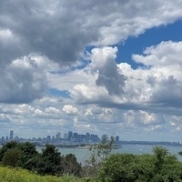 View from an island in Boston Harbor, with the city skyline in the distance and white, puffy clouds above.