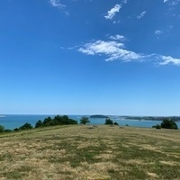 View from an island in Boston Harbor, with a meadow in the foreground, other islands in the distance, and a blue sky above.