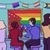 A drawing of Uhura and Spock from Star Trek SNW seated at the bar cheersing two purple drinks. They are both smiling and wearing their uniforms. Behind them is a rainbow vintage style United Federation of Planets flag with rainbow stripes. Around them are vague drawings that allude to the rest of the crew also being present, including Nurse Chapel and Number One. Art by @gravelyhumerus.