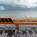 Auto-generated description: An orange bench is positioned on a wooden boardwalk overlooking a sandy beach and a cloudy seascape.