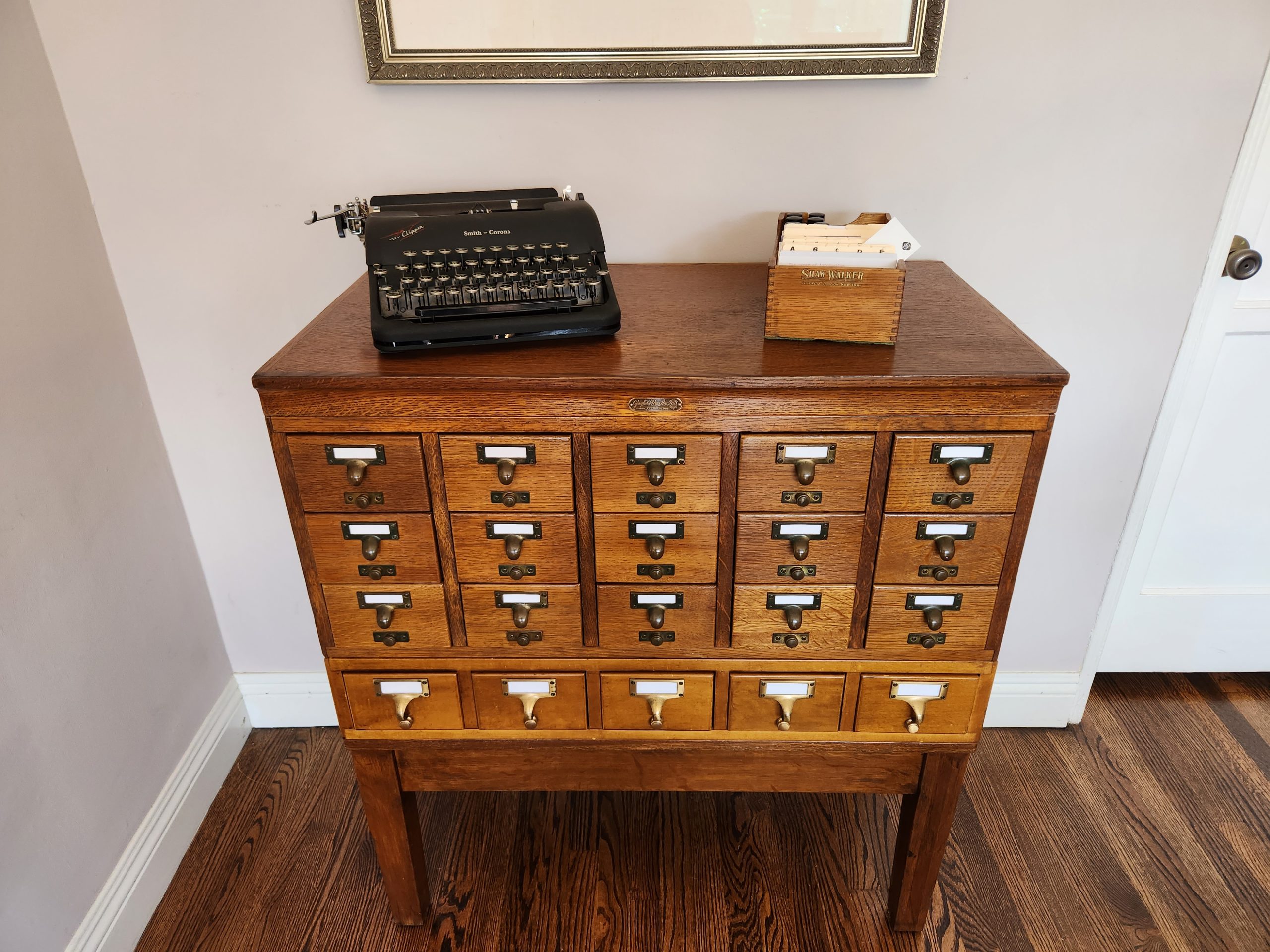 A waist high Gaylord Bros. library card catalog with a smaller desktop card index and black Smith-Corona Clipper typewriter on top.