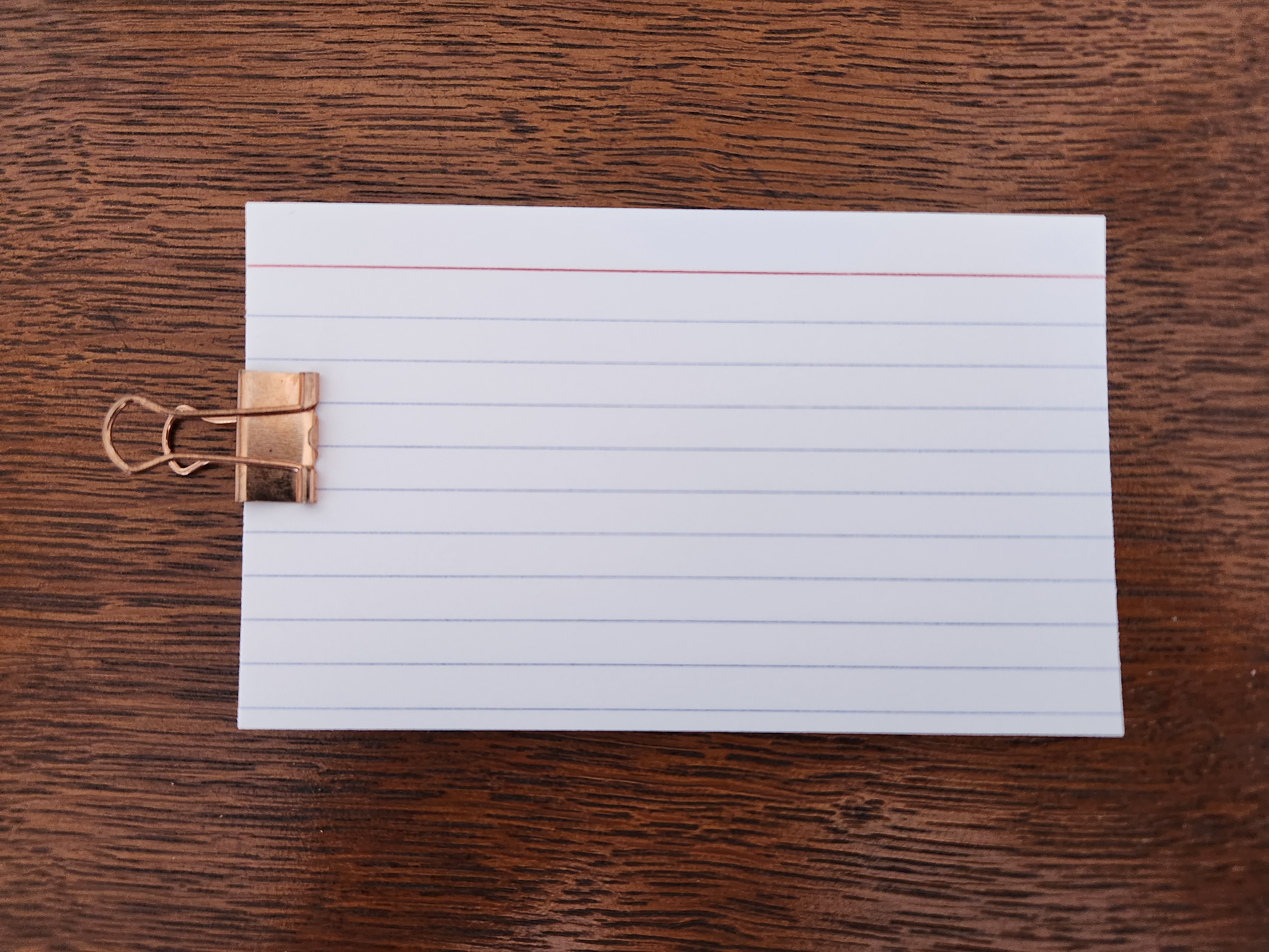 A stack of about 30 3 x 5 inch index cards with the traditional top red line and subsequent blue lines for writing all held together with a brass binder clip.