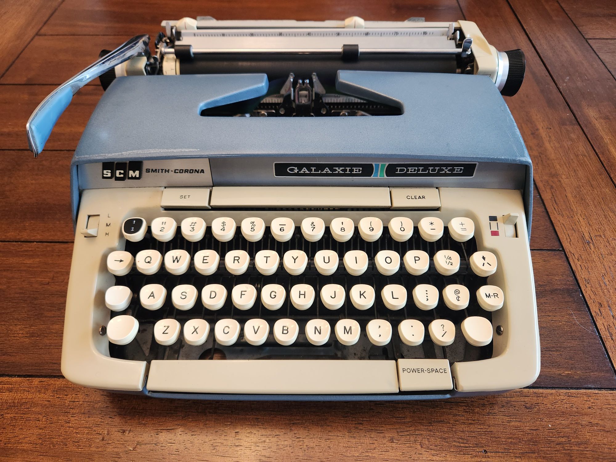 A view of a blue metal typewriter with a slightly yellowed plastic keyboard.
