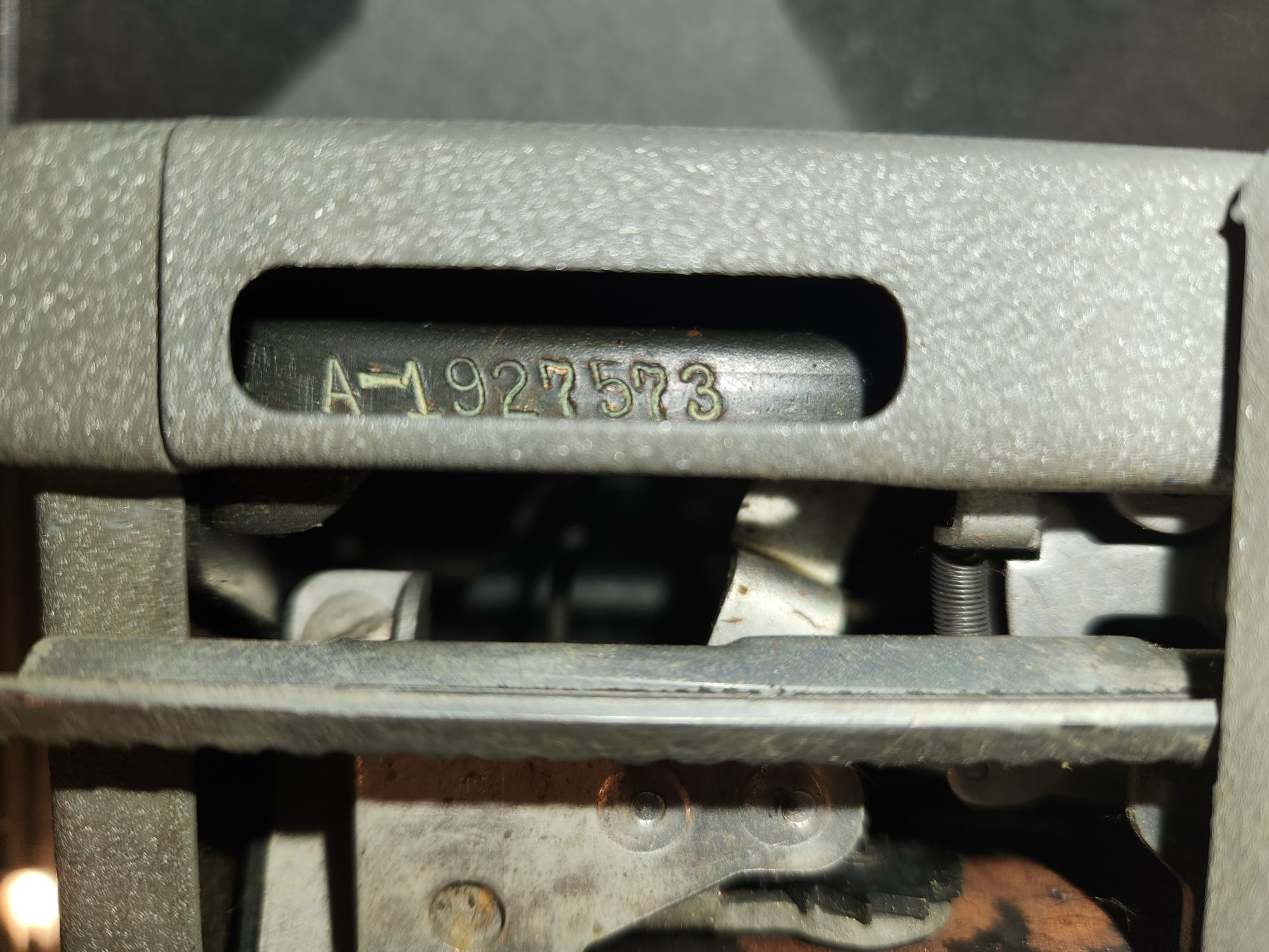 Serial number A-1927573 stamped into black metal recessed into the gray frame of the typewriter.