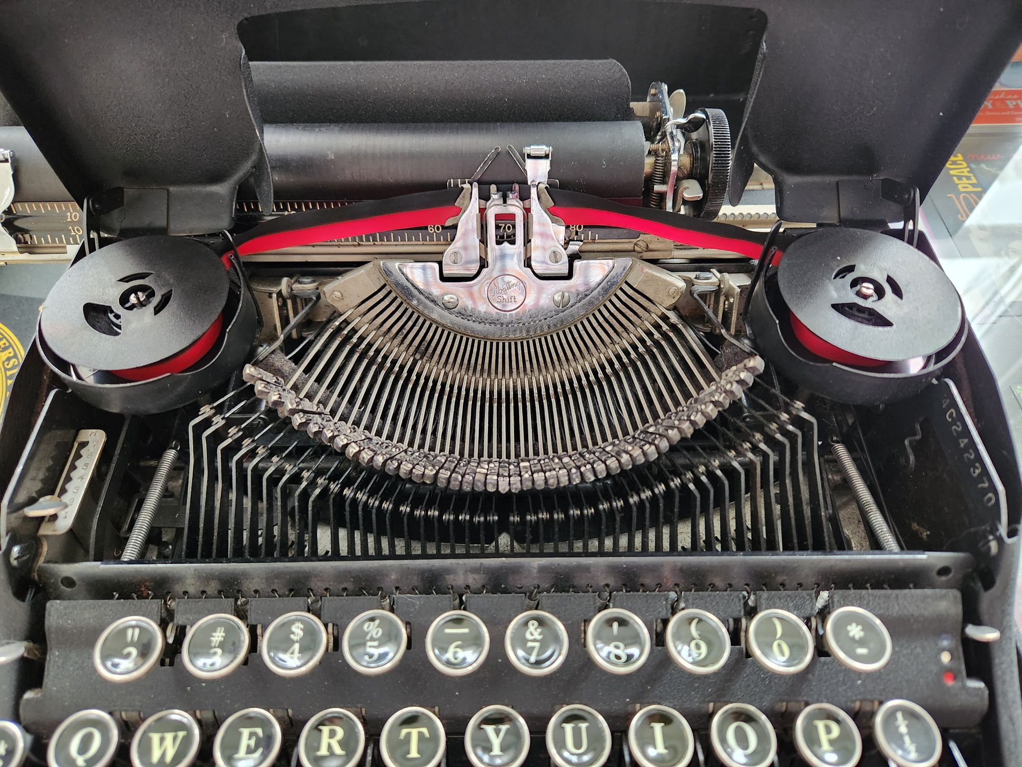 Two spools of black and red bichrome typewriter ribbon threaded into a Smith-Corona. In the foreground is the typebasket and two rows of glass keys.