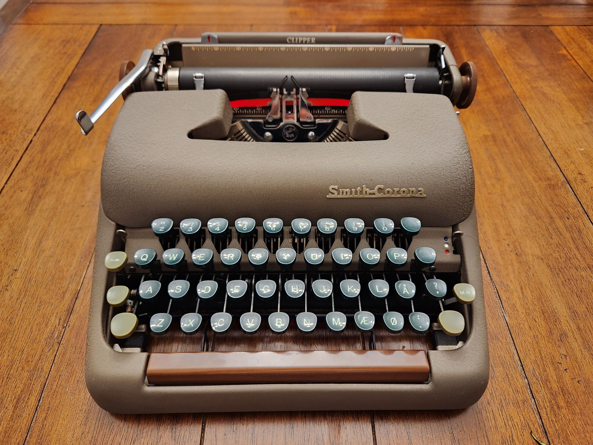 Angle down on the front of a brown Smith-Corona Clipper typewriter with green keys and a brown spacebar sitting on a wooden table.