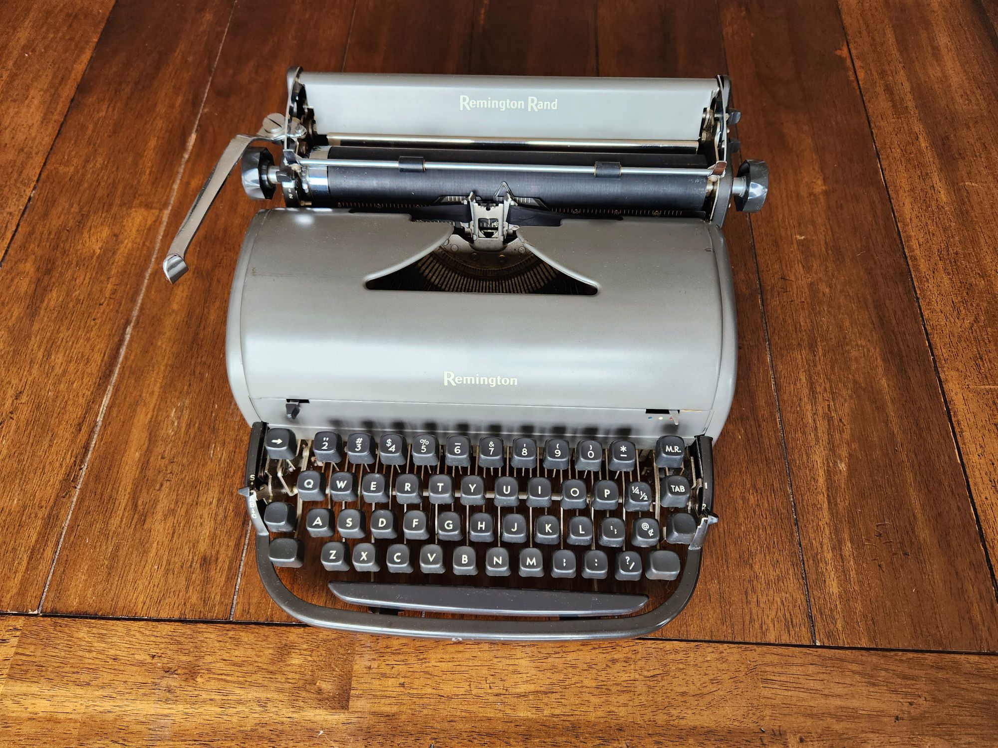 medium shot of a shiny gunmetal gray Remington All-New typewriter sitting on a wooden tabel