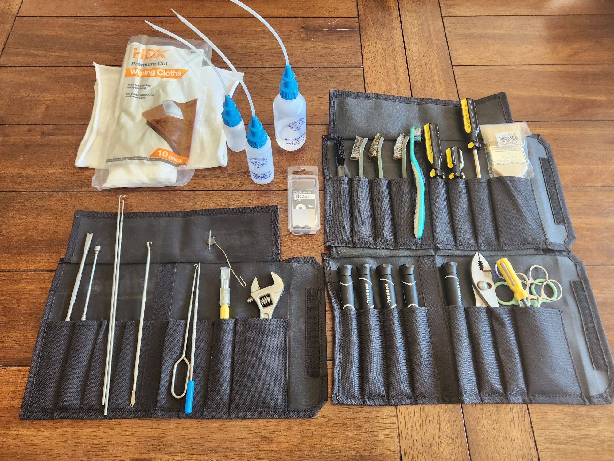 Three black nylon tool pouches filled with brushes, screwdrivers, wrenches, pliers and spring hooks for repairing typewriters. Above them are three plastic oiler bottles with long thin tube dispenser straws and some clean, white cotton cloth rags.