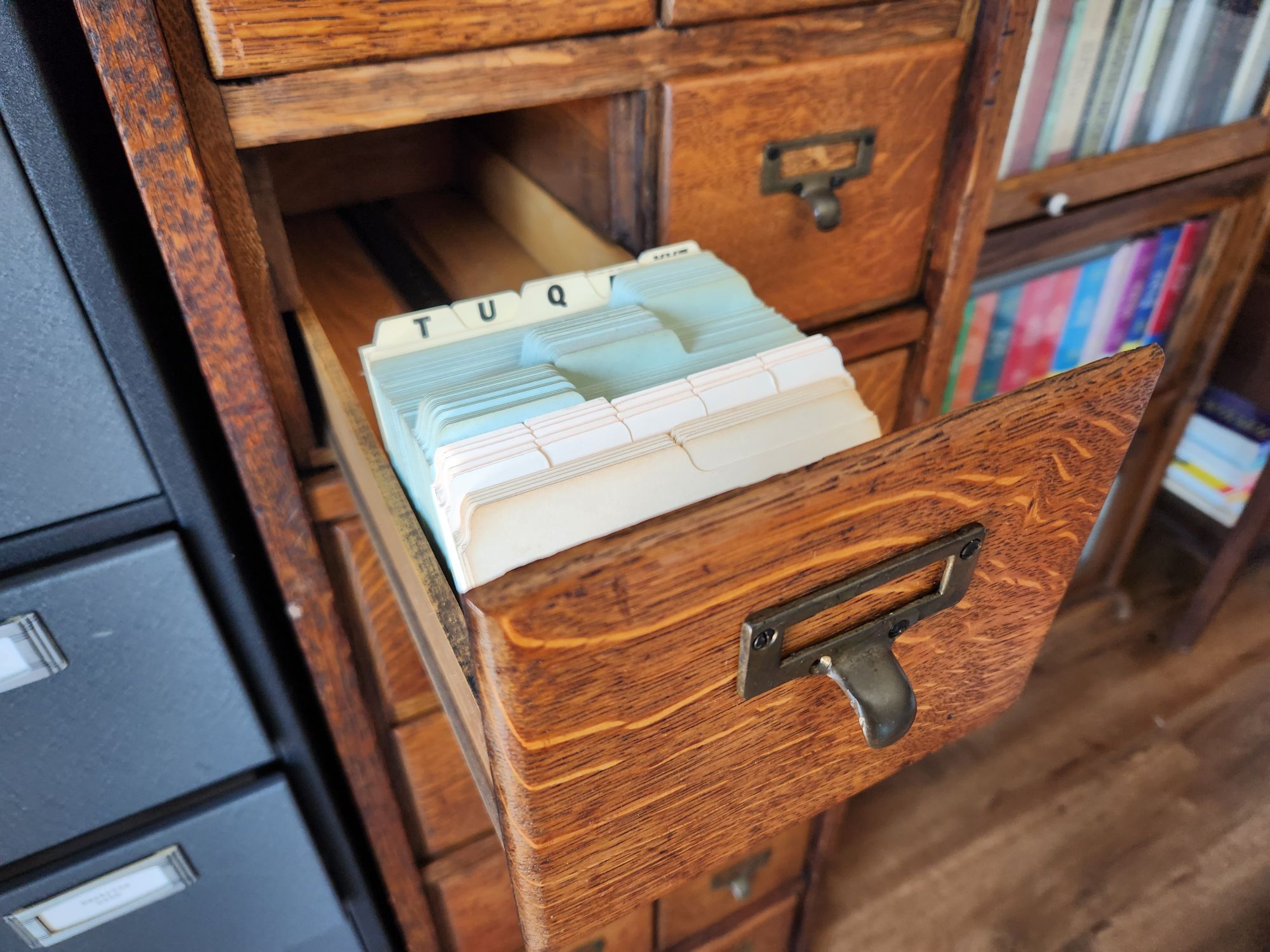 One drawer of a large oak card index opened up several inches displaying a variety of index card dividers.