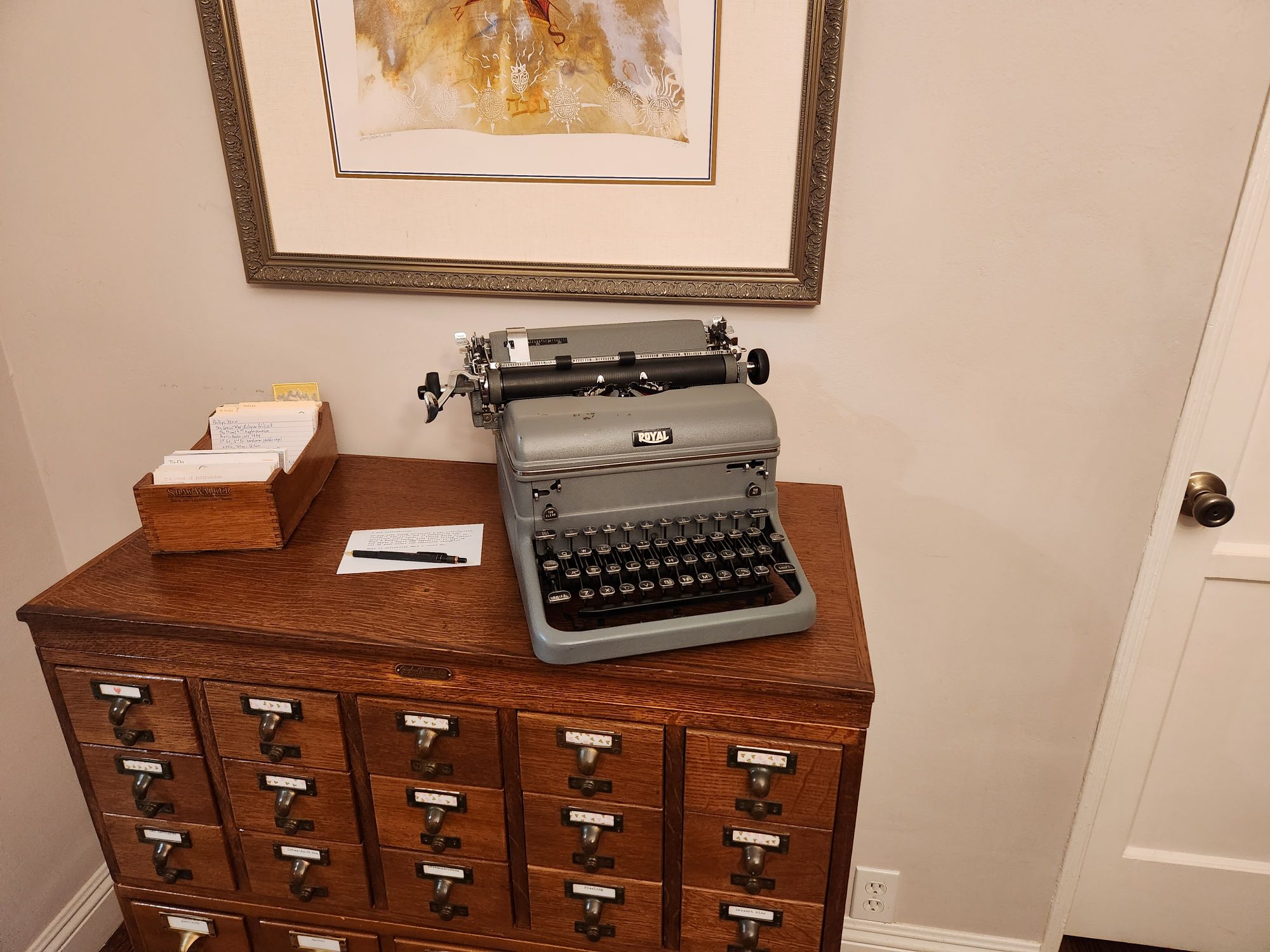 A gray 1950 Royal KMG typewriter on a wooden card catalog table next to a 10 inch card index tray with index cards in it