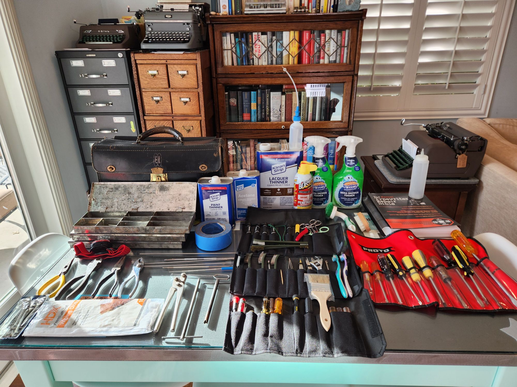 A large table covered with a repair bag and a wide variety of typewriter repair tools and solvents.