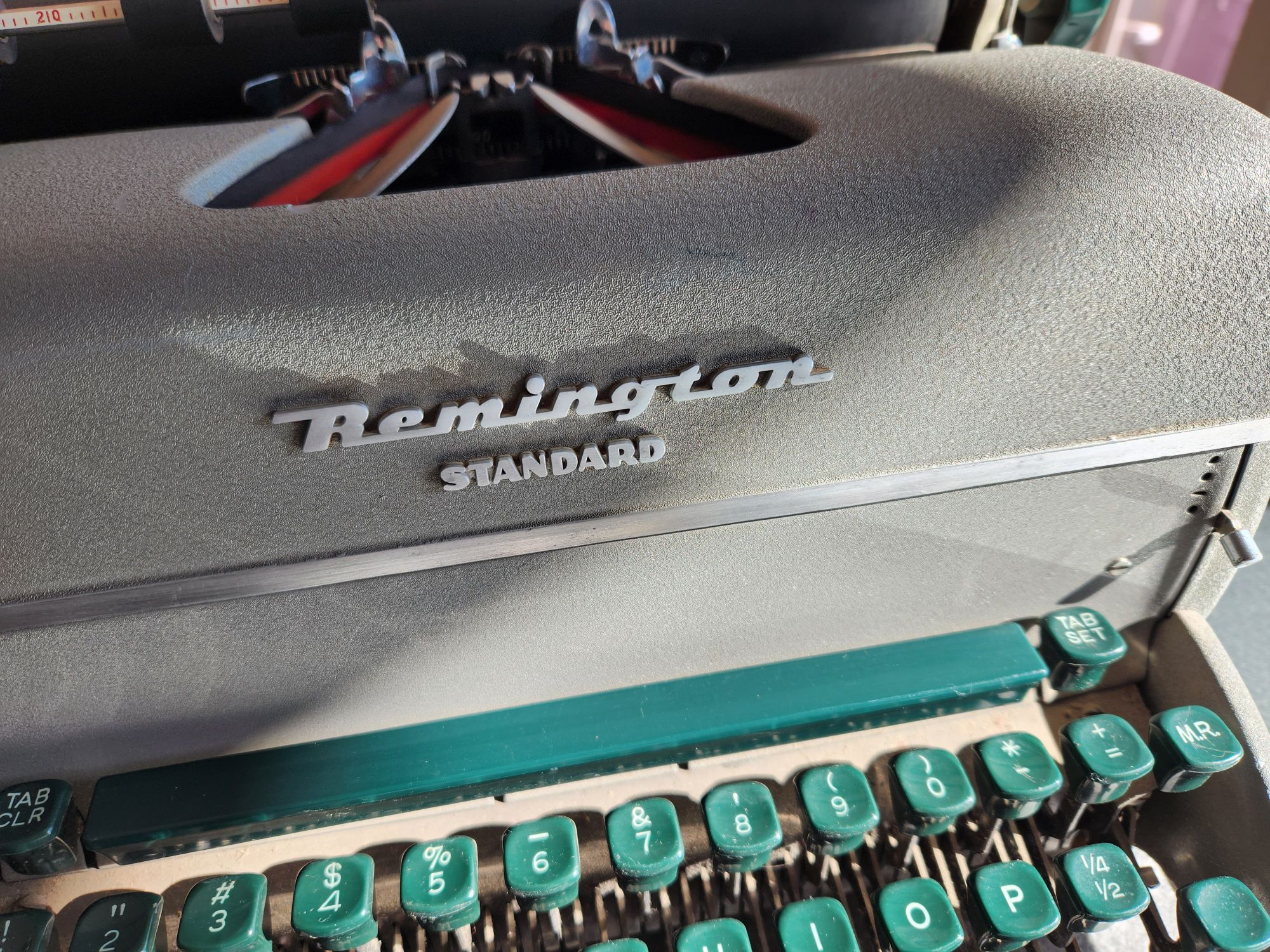 Shadows and sunshine play across the sparkling front of a gray Remington Standard typewriter with green keys