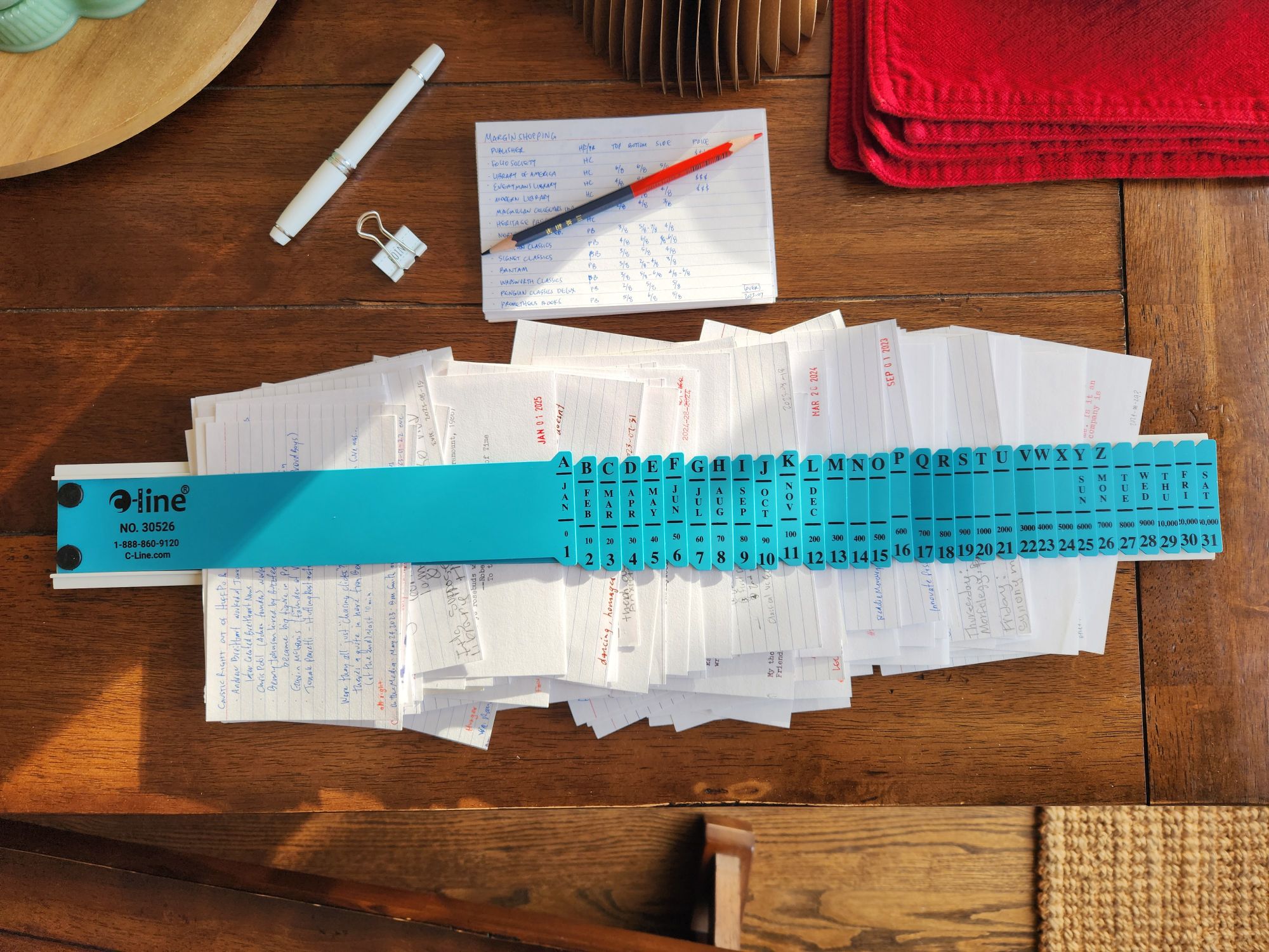View down onto a table with a C-line index card sorter with alphabetical tabs full of index cards. There are 31 various flaps labeled with letters of the alphabet, the months of the year, days of the week, and days in a month which can be used to quickly file index cards.