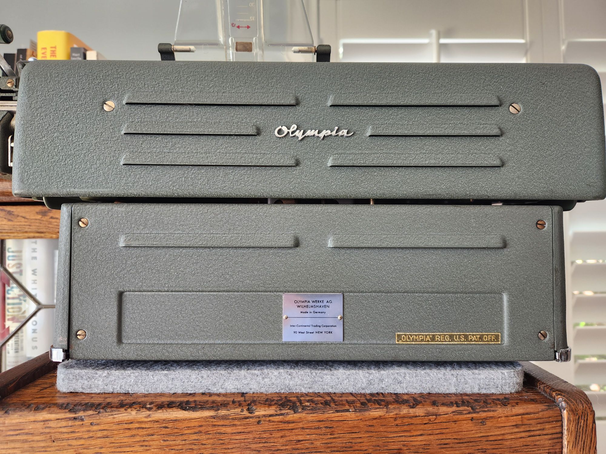 Rear of a green crinkle painted Olympia SG1. The bottom of the machine has a panel with a metal Olympia manufacturer's plate showing the company name, place of manufacture, and location of the dealer ship in New York. On either side is a wide rectangle where other identifiers could be similarly placed.