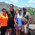 Four people posing together at a scenic overlook with a turquoise bay, sailboats, and green hillside in the background