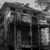 Abandoned brick building with a two-storey metal balcony and overgrown vegetation in black and white