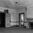 Derelict room with peeling paint, a wooden fireplace, and open doorways leading to dark interiors