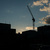 Silhouette of a construction crane rising above city buildings against a dusk sky with scattered clouds