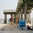 People walking barefoot on sand beneath a wooden pier, with a beach chair and bags nearby