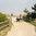 People walking along a sandy, fenced path towards a beach, one pulling a cart with gear
