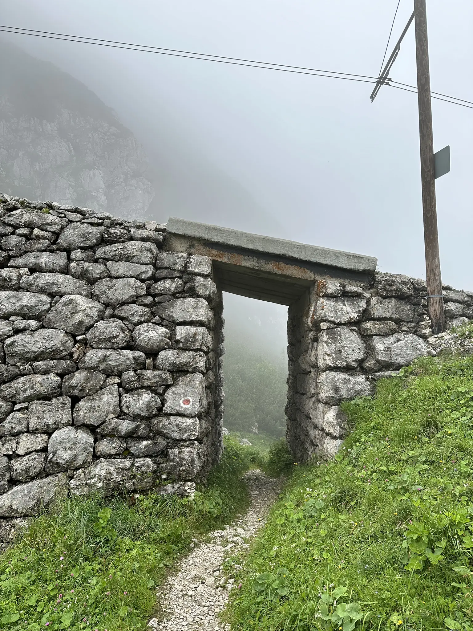 Steinernes Tor im Nebel, das auf einen schmalen Bergpfad führt.