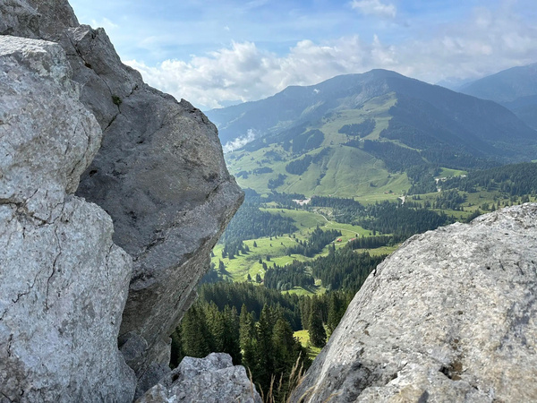Eine malerische Berglandschaft mit grünen Tälern und Felsen im Vordergrund unter einem blauen Himmel.