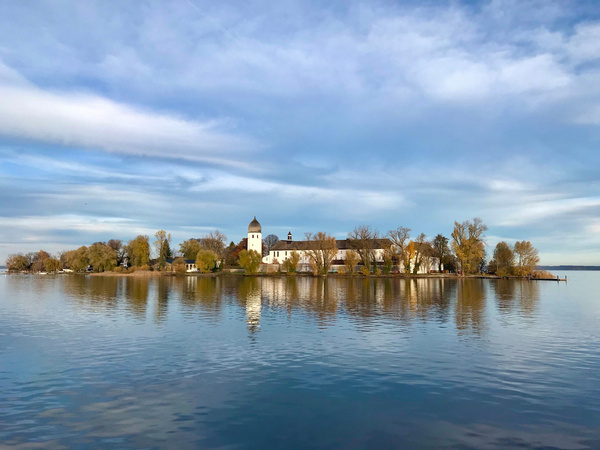 Die malerische herbstliche Fraueninsel spiegelt sich ruhigen Wasser des Chiemsee unter einem bewölkten Himmel.