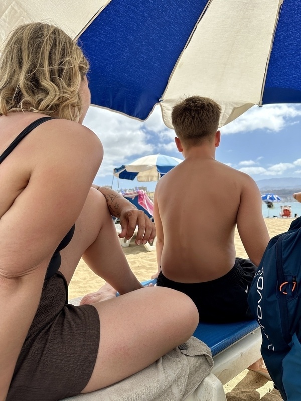 Eine Frau und ein Junge sitzen unter einem Sonnenschirm am Strand.