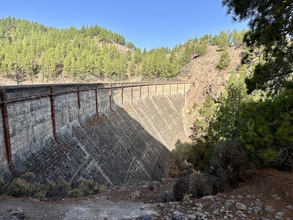 Die Staumauer des Presa de los Hornos umgeben von Bäumen in einer bergigen Landschaft.