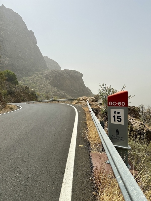 Eine kurvenreiche Bergstraße in Gran Canaria führt an einem Kilometerstein vorbei, umgeben von karger Landschaft und Felsen.