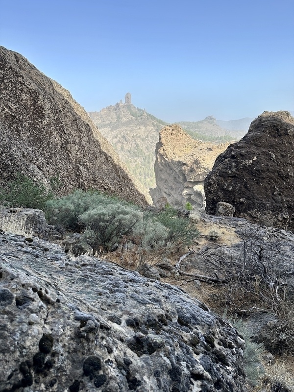 Eine felsige Landschaft mit trockener Vegetation, umgeben von hohen Felsformationen und einem blauen Himmel im Hintergrund.