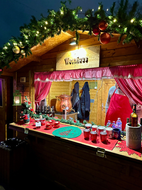 Ein festlich dekorierter Verkaufsstand mit einem „Weinhaus“-Schild auf einem Weihnachtsmarkt in Sofia bietet verschiedene Getränke und weihnachtliche Dekorationen an.