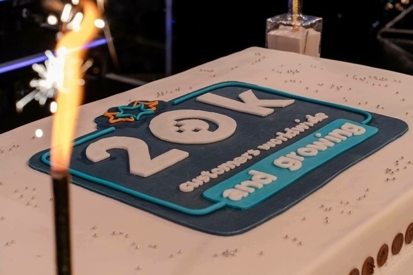 A celebratory cake features a design with 20k customers worldwide and growing written on it, surrounded by sparklers.