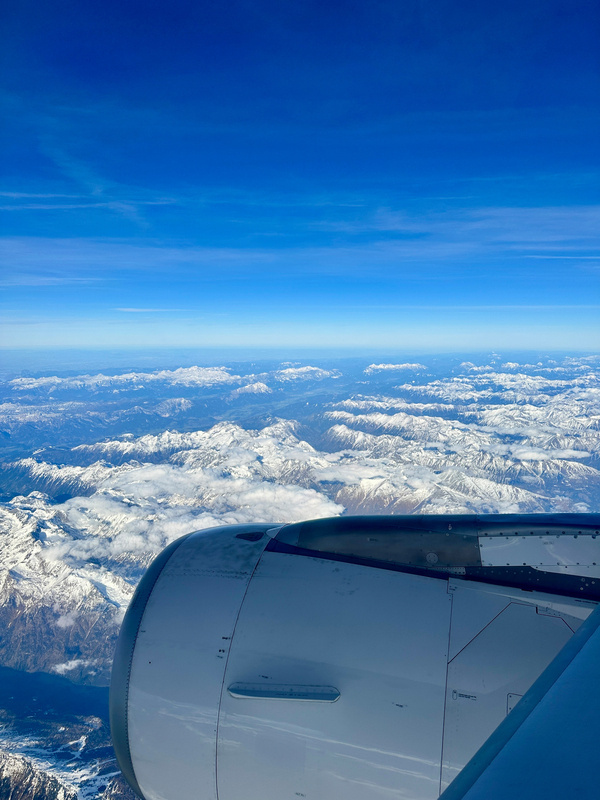 Ein Flugzeug fliegt über die schneebedeckte Gipfel der Alpen bei Graz, unter einem klaren blauen Himmel.