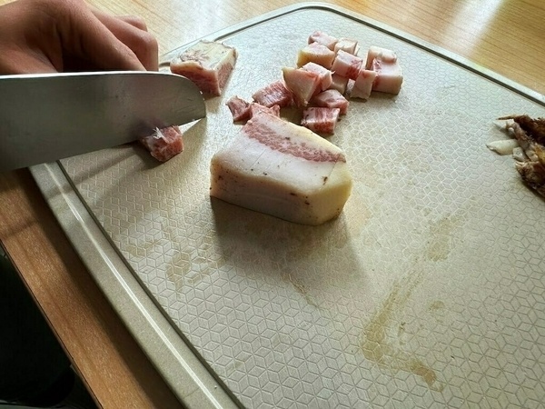 Auf einem Schneidebrett wird Speck in Würfel geschnitten.