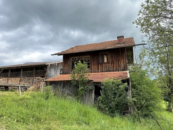 Ein rustikales Holzgebäude mit rotem Ziegeldach steht inmitten grüner Landschaft unter bewölktem Himmel.