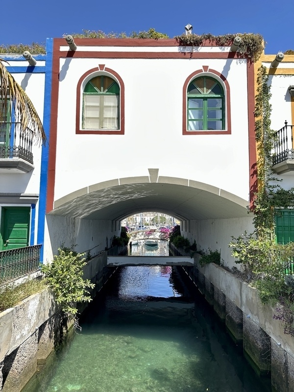 Ein charmanter Kanal fließt unter einer Brücke mit einem weiß-rot-blau eingerahmten Gebäude und grünen Fenstern hindurch.