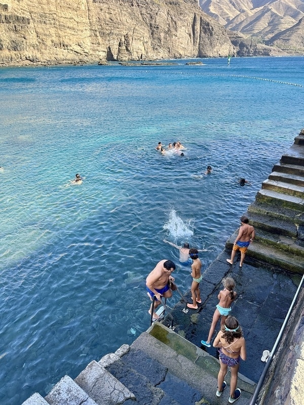 Eine Gruppe von Menschen genießt das Schwimmen an einem Felsufer mit klarem blauem Wasser und steinernen Treppenstufen.