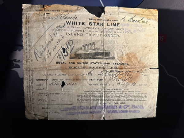 Ein altes Ticket der White Star Line für die Überfahrt auf der Titanic ist abgebildet, mit handschriftlichen Notizen und Stempeln versehen.