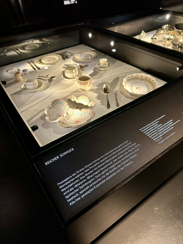 Ein Set aus elegantem Geschirr und Besteck der ersten Klasse der Titanic wird in einer beleuchteten Vitrine präsentiert.
