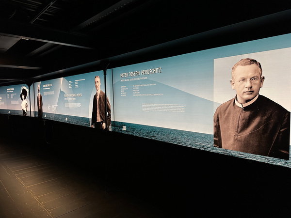 Porträtfotos und Informationen über Reisenden der Titanic sind auf einer Ausstellungswand dargestellt.