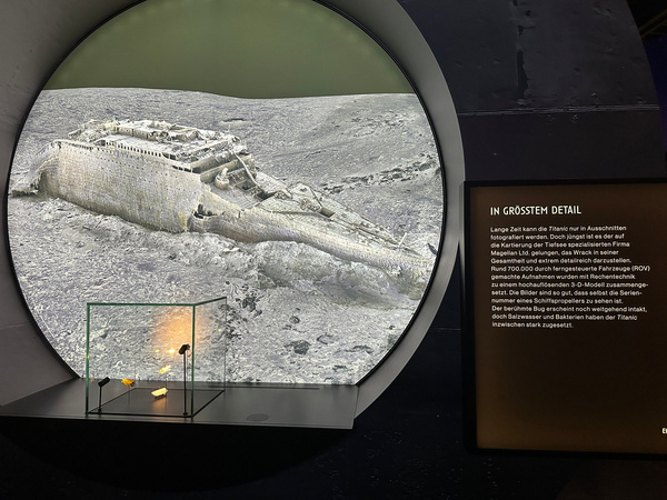 Ein großer Bildschirm zeigt das Wrack der Titanic auf dem Meeresgrund, begleitet von einer Infotafel mit Hintergrundinformationen.