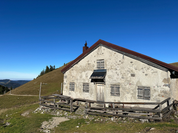 Die geschlossene Jägerbauernalm auf einem Hügel unter einem klaren blauen Himmel.
