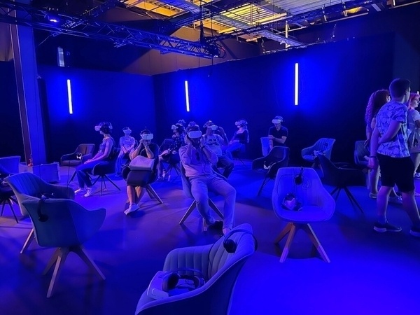 Menschen sitzen in einem blau beleuchteten Raum der Titanic-Ausstellung in München und tragen Virtual-Reality-Headsets.