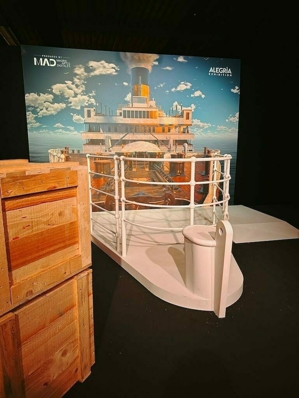 Eine 3D-Installation zeigt das Deck der Titanic mit einem Hintergrund aus Himmel und Wolken, flankiert von Holzkisten.