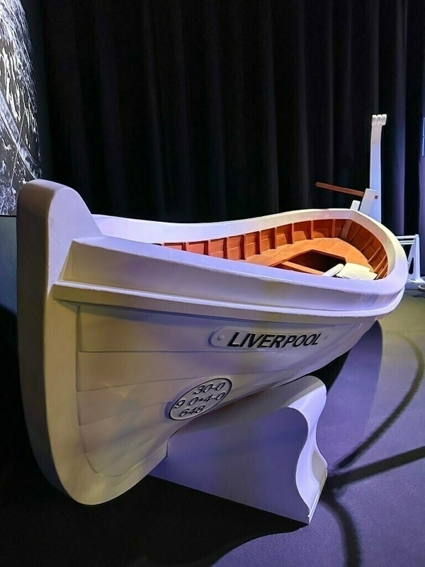 Ein weißes Rettungsboot der Titanic mit der Aufschrift Liverpool steht in einem dunklen Raum.