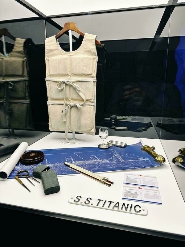 Ein ausgestelltes Set von Original Artefakten der Titanic, darunter eine Rettungsweste, ein Plan der Titanic, ein Glas und verschiedene nautische Werkzeuge.