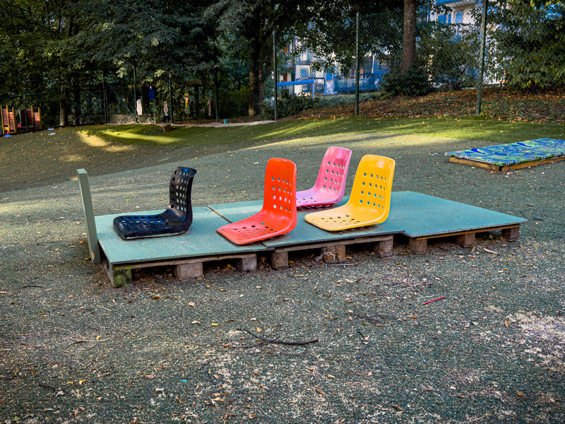 Four colorful plastic seats are arranged on a wooden platform in an outdoor park setting.